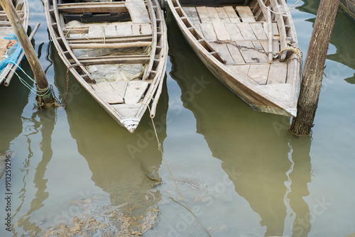 Fototapeta wooden rowboats moored to wooden poles in murky water