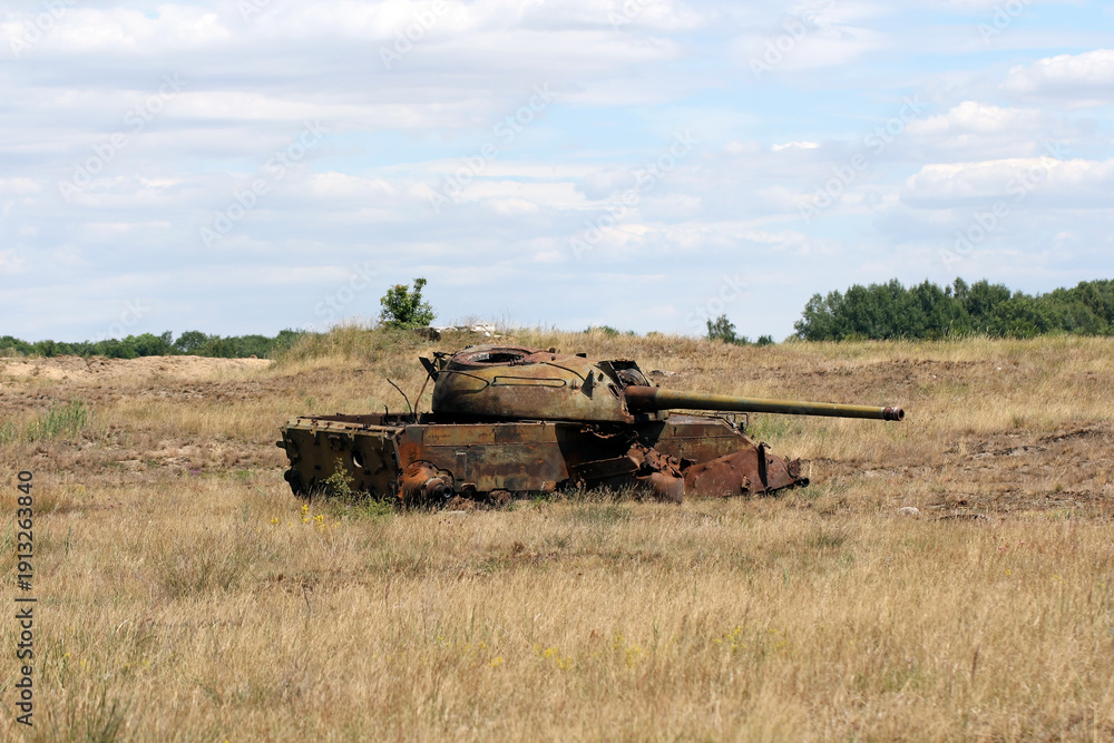 Fototapeta premium A destroyed, rusting tank in a meadow. A battlefield, war, a combat training ground.