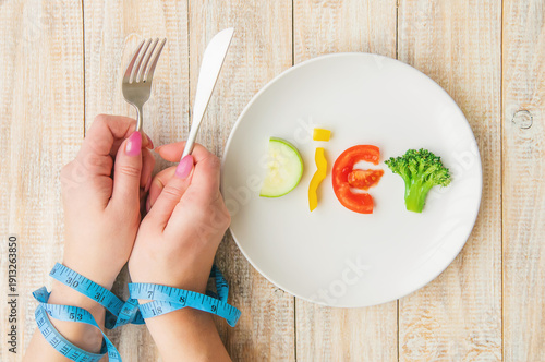 Photography Hands tied with blue measuring tape holding fork and knife over vegetable word d