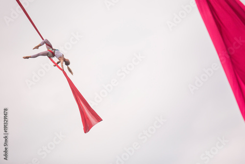 Bild auf Leinwand Aerial silk session in a park, featuring a performer upside down on red silks du