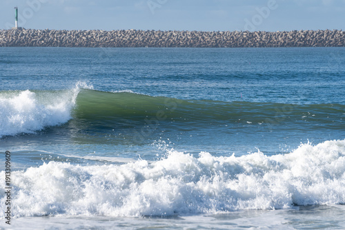 Beautiful turquoise ocean waves rolling toward the shore under a soft, cloudy sky. A serene and refreshing view of the sea's natural movement and spray.