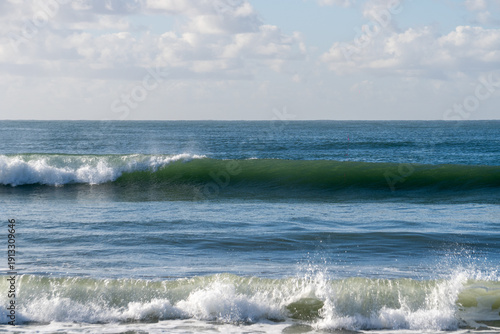 Beautiful turquoise ocean waves rolling toward the shore under a soft, cloudy sky. A serene and refreshing view of the sea's natural movement and spray.