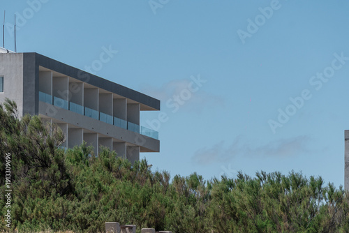 Modern concrete house overlooking coastal vegetation under a clear blue sky, blending clean architectural lines with natural surroundings.