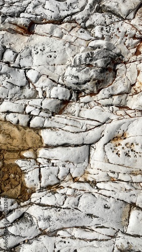 Natural white rock texture with cracks, veins, and layered geological patterns. Close-up of weathered limestone surface with brown mineral deposits and embedded pebbles. Abstract stone background suit