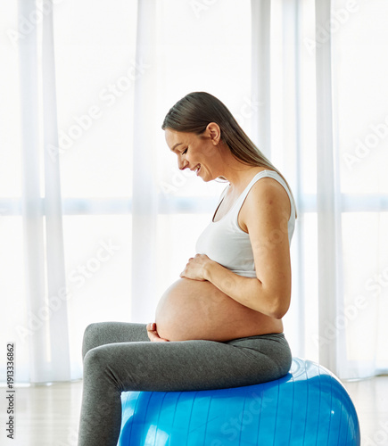 Free Download Portrait of a young happy pregnant woman doing exercise with a ball at home or in a gym - GFXLoad