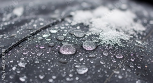 Close up of transparent water droplets and melting snow crystals on dark waterproof fabric with visible stitching, macro shot with shallow depth of field and blurred background. Concept of water resis