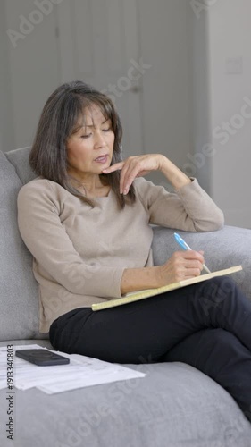 Business woman writing communication list on note pad working at home sitting on living room sofa alone vertical video