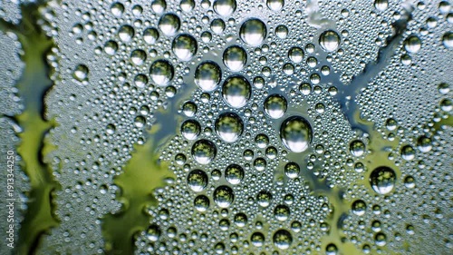 Condensation forms countless clear droplets on a textured surface some magnifying the blurry green and dark shapes of an underlying environment