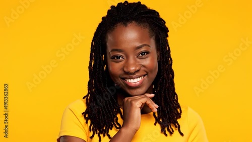 Portrait of smiling Black woman with locs and finger on chin against vibrant yellow background