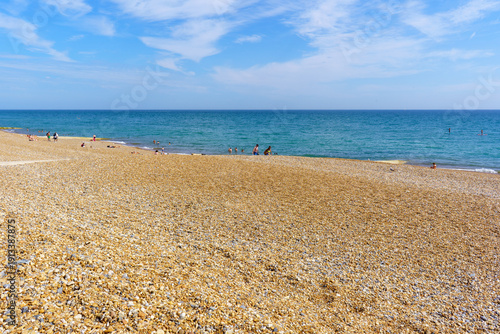 A shingle beach in Brighton (England) meeting a calm ocean under a bright sky.