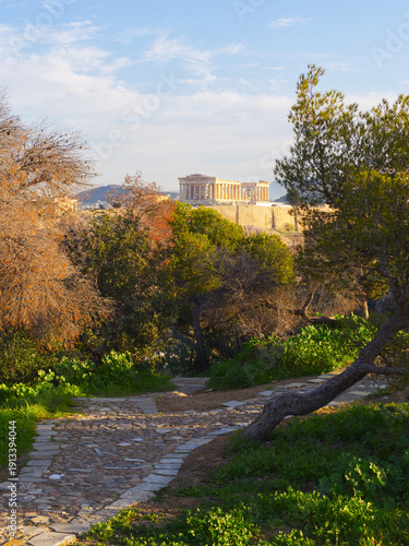 Stone pathway through lush park with ancient Acropolis and Parthenon temple visible in background