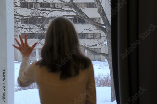 Woman looking through window. Woman silouhette in front of an interior window. Woman social health. Mental health and solitude. Woman social problem.