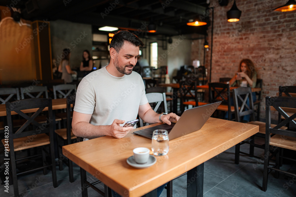 Fototapeta premium Freelancer working on laptop and using smartphone in cafe