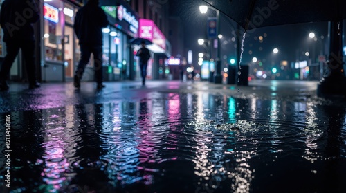 Wallpaper Mural Low angle puddle reflection of neon lights on a rainy city sidewalk at night with raindrops impacting and rippling the mirrored surface as blurred pedestrian silhouettes pass Torontodigital.ca