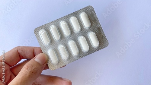 Fotografie A hand holding a blister pack containing white medication tablets against a clean white background