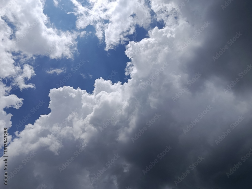 Obraz premium Dramatic Cloudscape with Blue Sky and Dark Storm Clouds, Weather Contrast Background, Moody Atmospheric Nature Scene