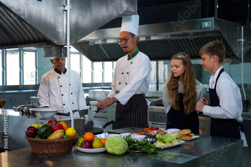 Chef teacher teaches cooking to the group children in class kitchen room.  Chef preparing student for learning marking and cooking food at workshop.  Education Concept