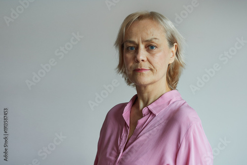 Portrait of an older woman in a pink shirt on a gray uniform background