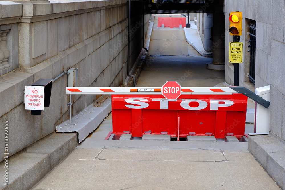 Fototapeta premium Warning STOP signs, closed automatic barrier and traffic lights accentuate the message to halt at the entrance of building garage.