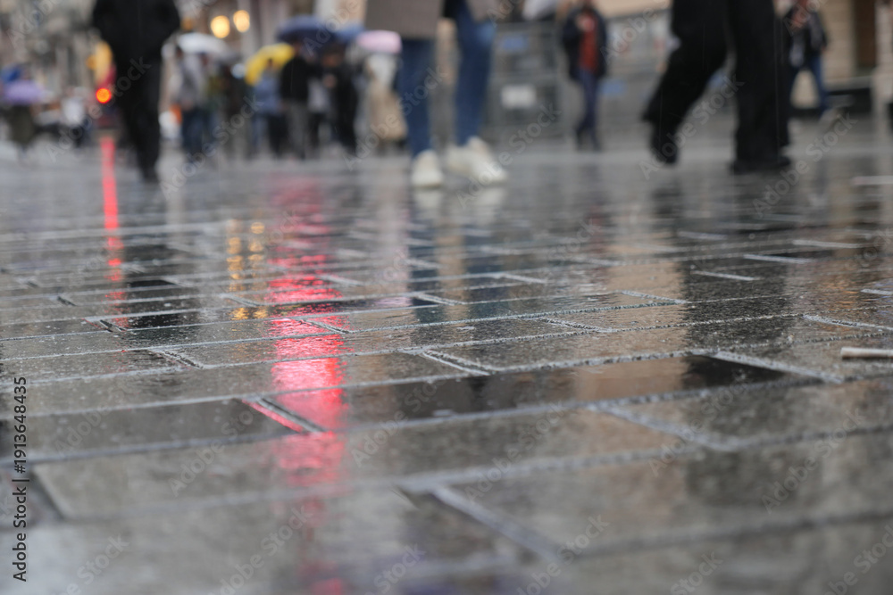 Fototapeta premium People walk on wet pavement in the city during rain