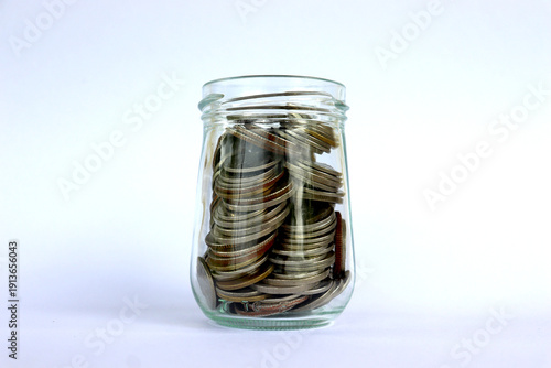 A coin in a glass jar, against a white background, financial concepts, investment, saving.
