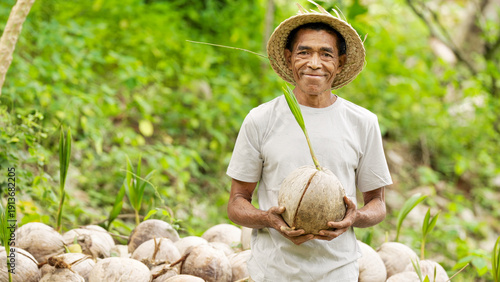Indonesian man farmer smiling portrait with coconut seedling on farm, field, or plantation, looking at camera, wearing straw hat, on flores island, indonesia, southeast asia, asian people