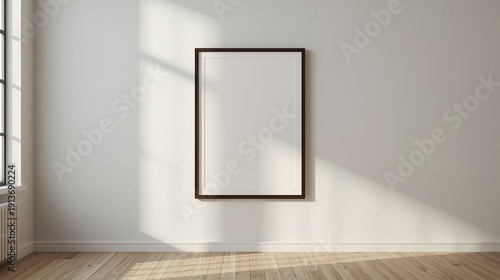 Empty black frame on a white wall in a minimalist room with sunlight and shadows.
