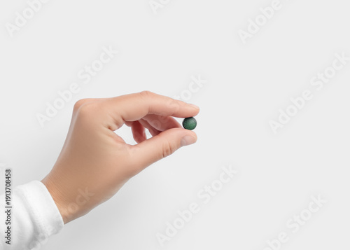 Hand holding a small round green detox pill