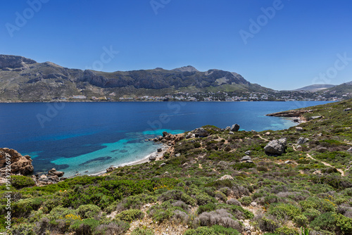 Rugged and lush landscape, beaches, coastline and the Aegean Sea on Telendos island in Greece on a sunny day. Mountainous Kalymnos island is in the background.