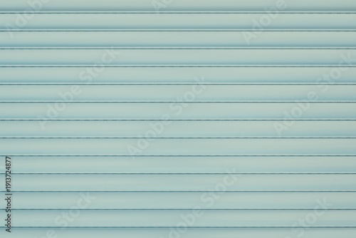 Light blue metal roller shutter background with horizontal parallel lines. Abstract pastel texture of protective window blind or garage door for industrial and architectural design.