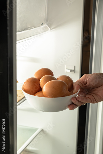 Hand placing a bowl of fresh brown eggs into a refrigerator for storage at home