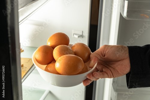 Hand placing a bowl of fresh brown eggs into a refrigerator for storage at home