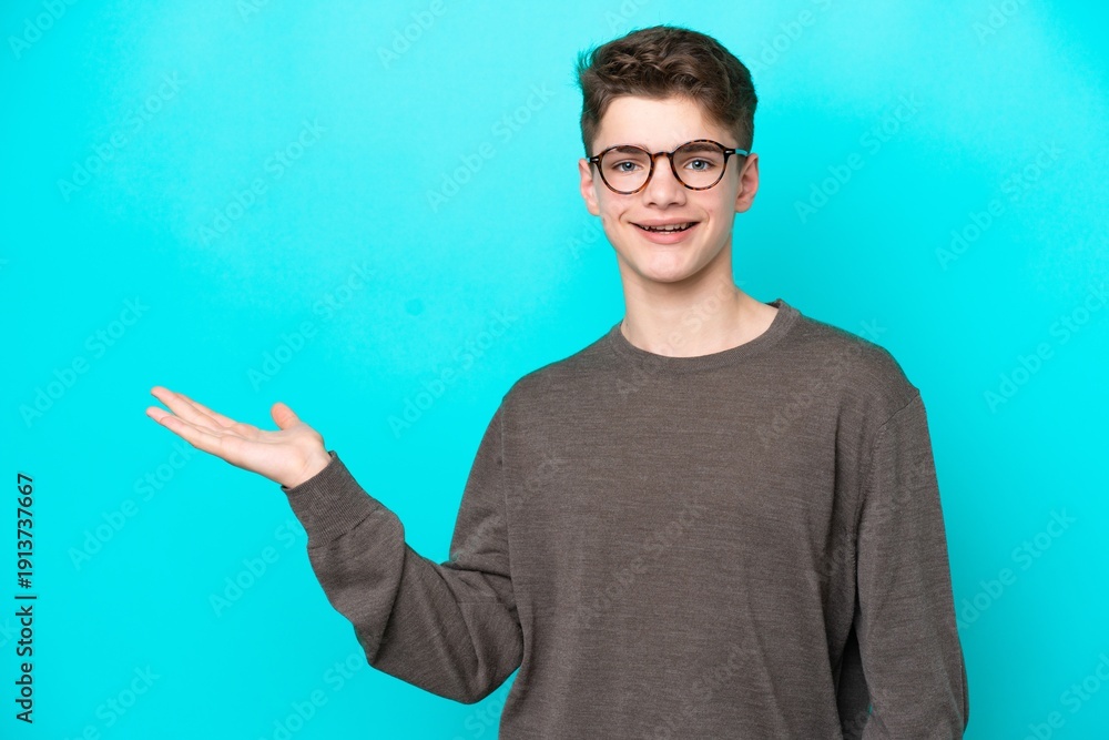 Fototapeta premium Teenager Russian man isolated on blue background holding copyspace imaginary on the palm to insert an ad