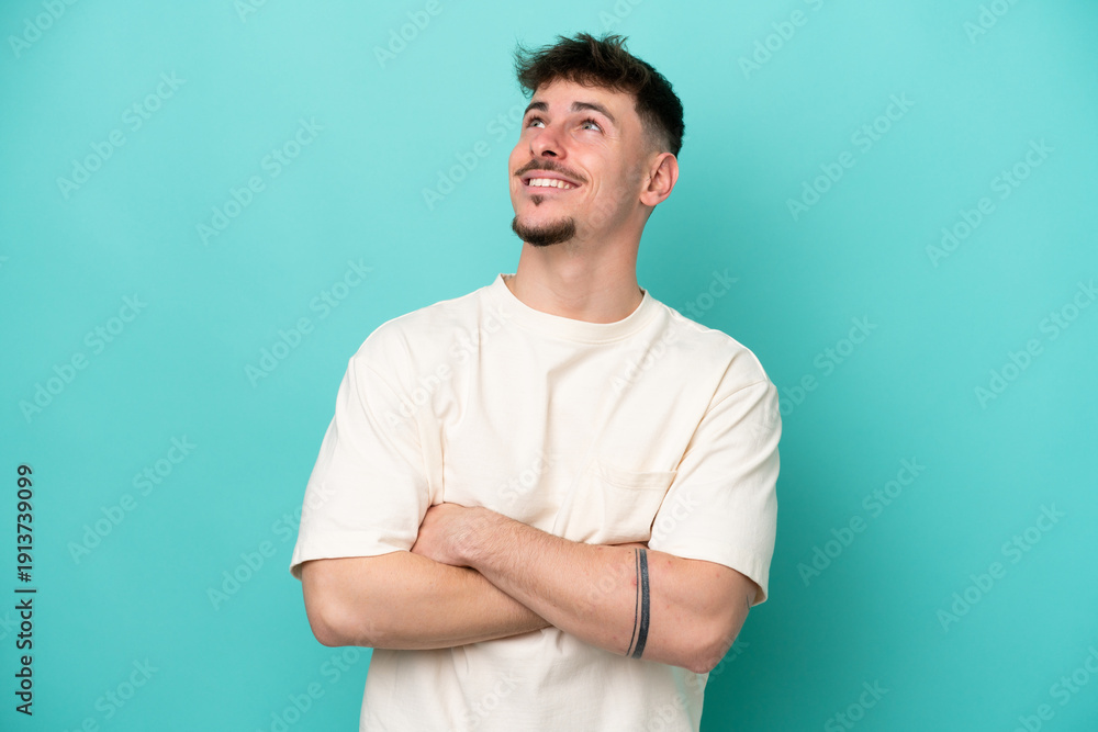 Fototapeta premium Young caucasian handsome man isolated on blue background looking up while smiling