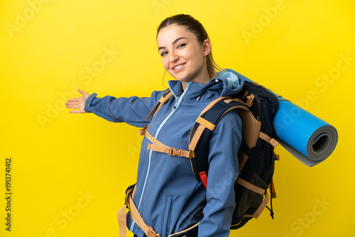 Fotografie Young mountaineer woman with a big backpack over isolated yellow background exte