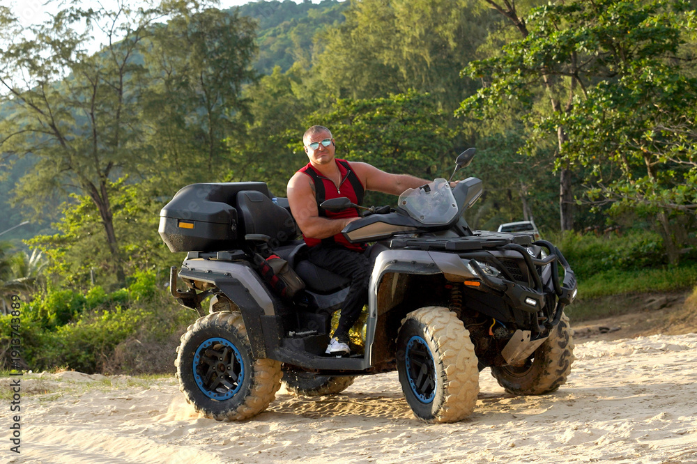 Fototapeta premium A man engages in extreme ATV riding on sand beach early in the morning