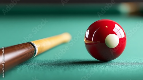 Red billiard ball with white dot positioned on green felt table beside a wooden cue stick, showcasing a close-up view of the game setup
