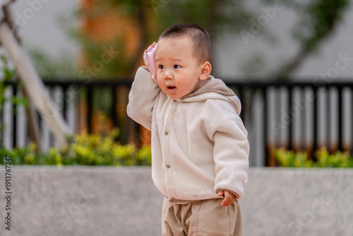 Fotografie Asian child playing with a toy phone outdoors, pretending to talk