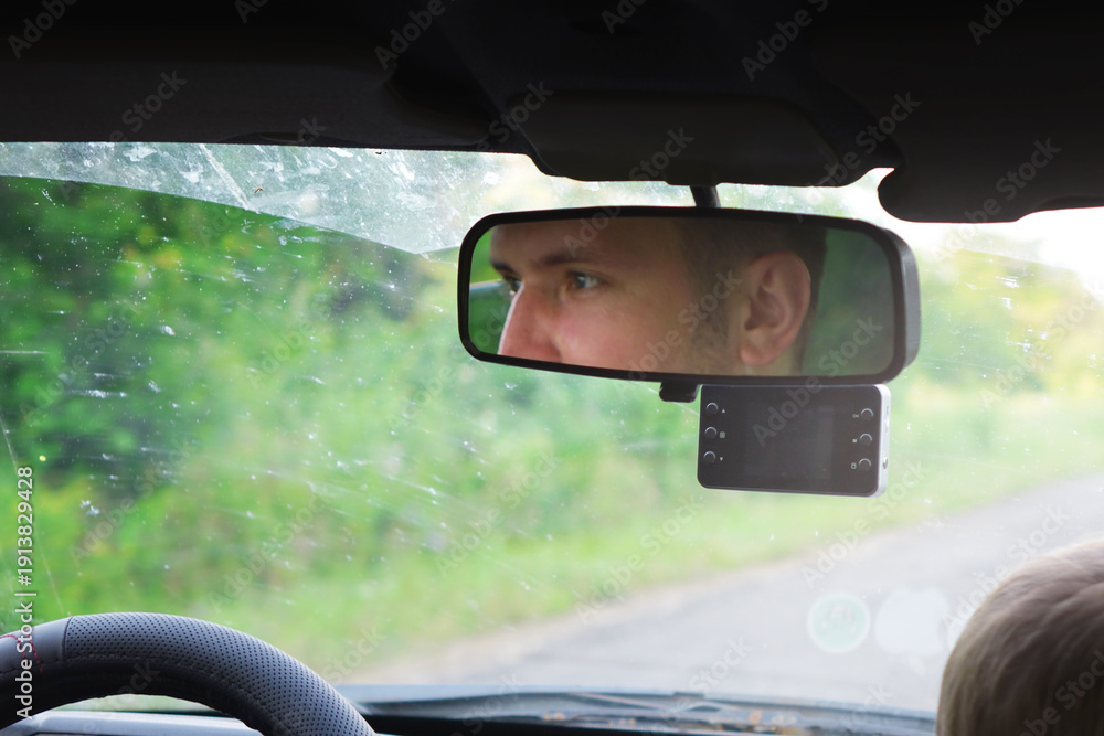 Naklejka premium Reflection of a young man's eyes in a car rearview mirror during a summer road trip