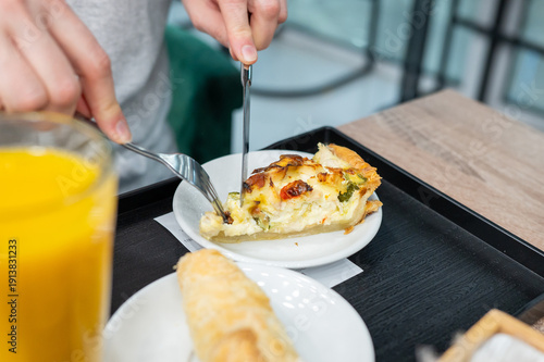Foto Person eating quiche in café with orange juice and pastry on tray