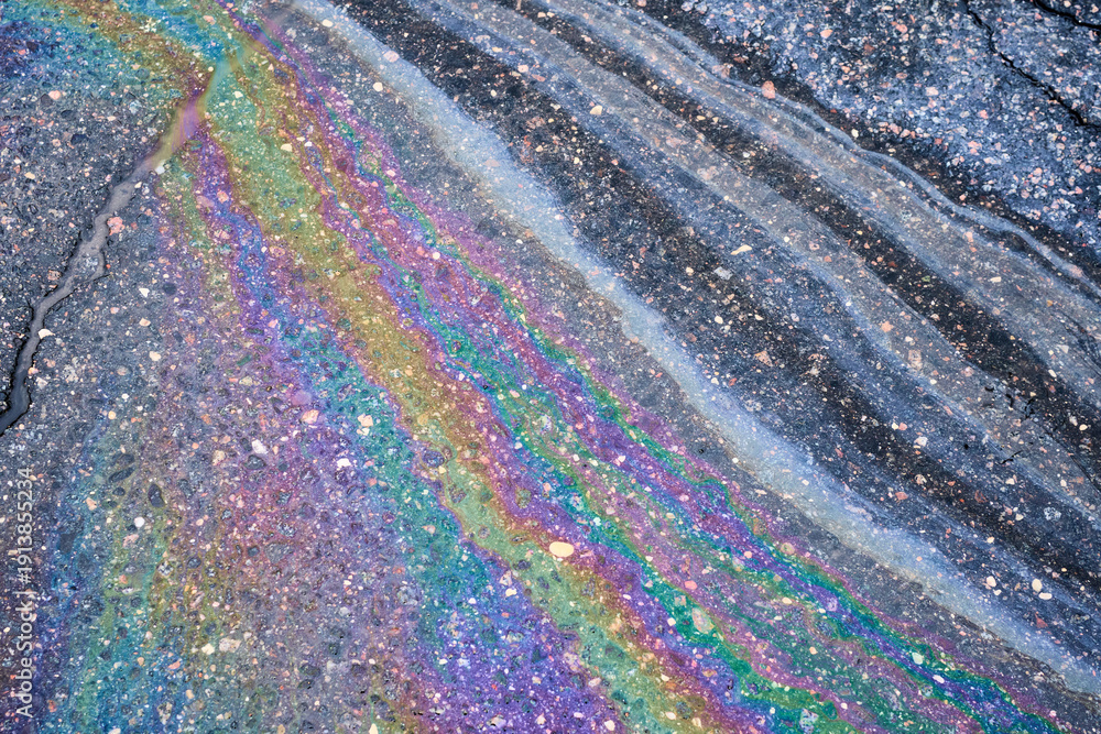 Fototapeta premium Oil slick creating vibrant rainbow patterns on a wet asphalt road, highlighting the beauty and danger of fuel spills