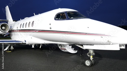 white luxury business jet sits tarmac night illuminated by bright ramp lighting fuselage cockpit windows nose landing gear rear mounted engine against hangar illumination aircraft aviation 