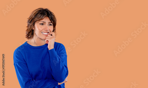 Fotografia Woman looks worried while biting her nails in front of an orange background in a
