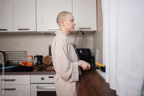 Schilderij op canvas bald woman in a soft bathrobe carefully peeling an orange in her home kitchen, s