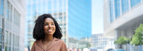 Tableau sur toile Happy confident smiling young African American professional woman, student, female entrepreneur businesswoman manager looking away standing outdoors on business city street dreaming of career success