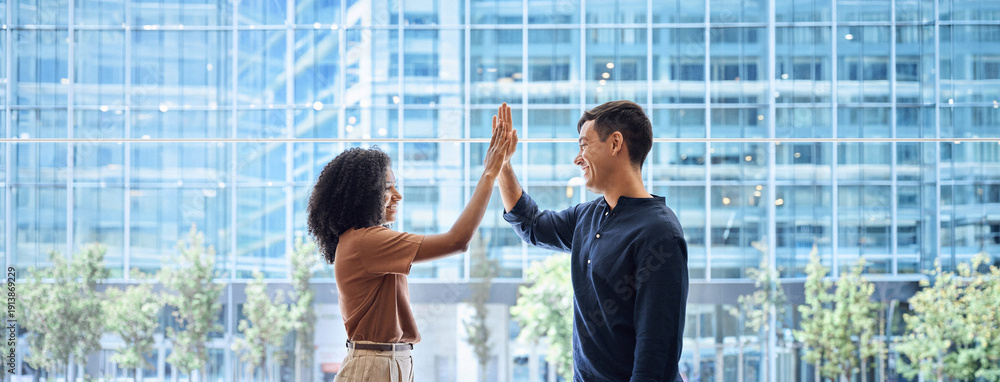Obraz premium Happy diverse young team business people, two colleagues man and woman employees giving high five standing in office as concept of corporate success, leadership in teamwork, professional achievement.