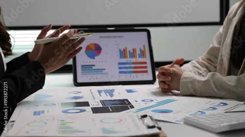 Businesswoman discussing financial data during a meeting. Financial advisors analyzing charts and graphs on a tablet and paper reports. Two colleagues working together on a business strategy.