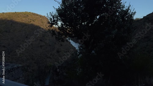 Sunlit canyon road drive with winding river and trees