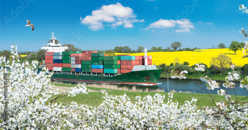 Spring landscape with cherry blossom and rapeseed blossom as well as a container ship on a canal 