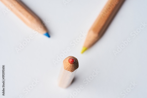 Top View of Three Colored Pencils Pointing to a Red Pencil End on White Background
